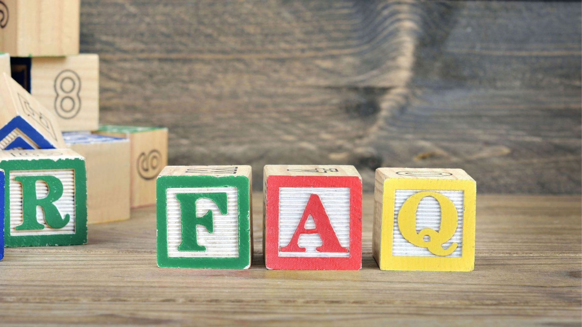 Colorful wooden blocks spelling out 'FAQ' on a textured wooden surface, symbolizing frequently asked questions about renal cancer treatment costs. The blocks are in focus in the foreground with a blurred stack of other blocks in the background, suggesting a resource for information and answers.