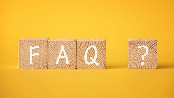 Three wooden blocks against a yellow background spell out "FAQ" with the last block featuring a question mark, symbolizing frequently asked questions about stomach cancer therapy financing. This image could lead to a section that provides answers to common inquiries regarding the expenses involved in treating stomach cancer.
