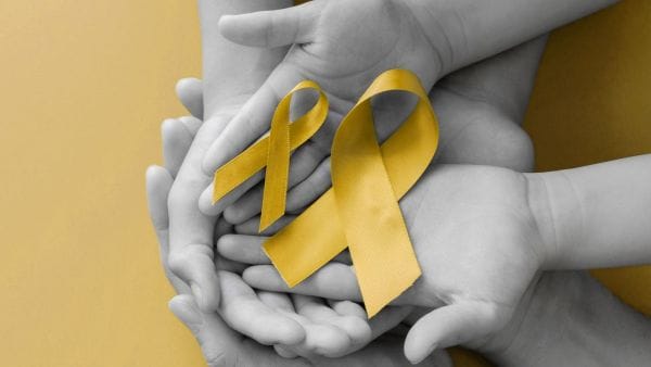 Several hands of varying ages holding yellow ribbons, symbolizing support for Sarcoma cancer awareness and the financial burden of treatment costs.