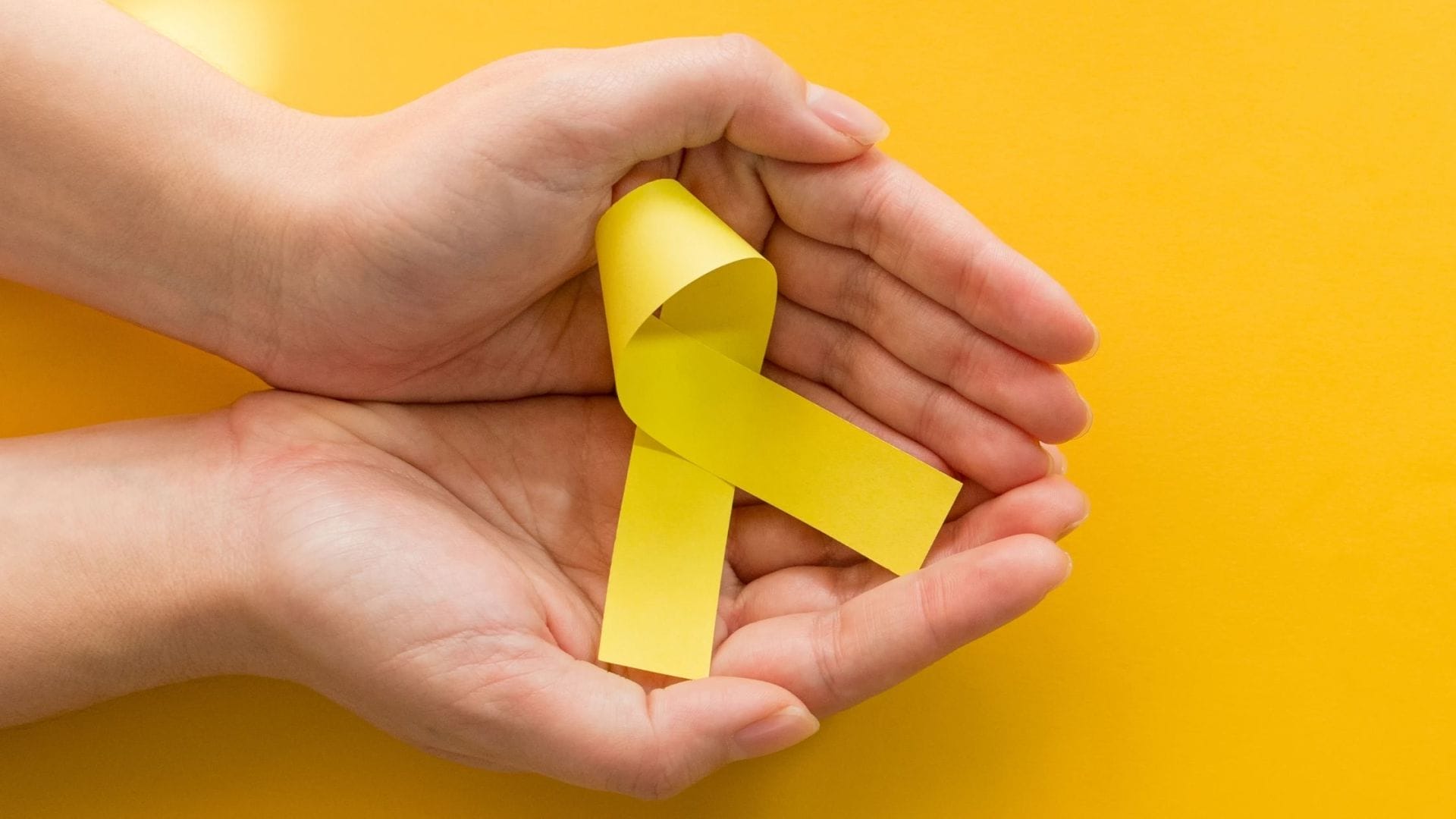 Hands carefully holding a yellow ribbon, symbolizing support for those managing sarcoma cancer treatment costs and raising awareness for the financial resources available.