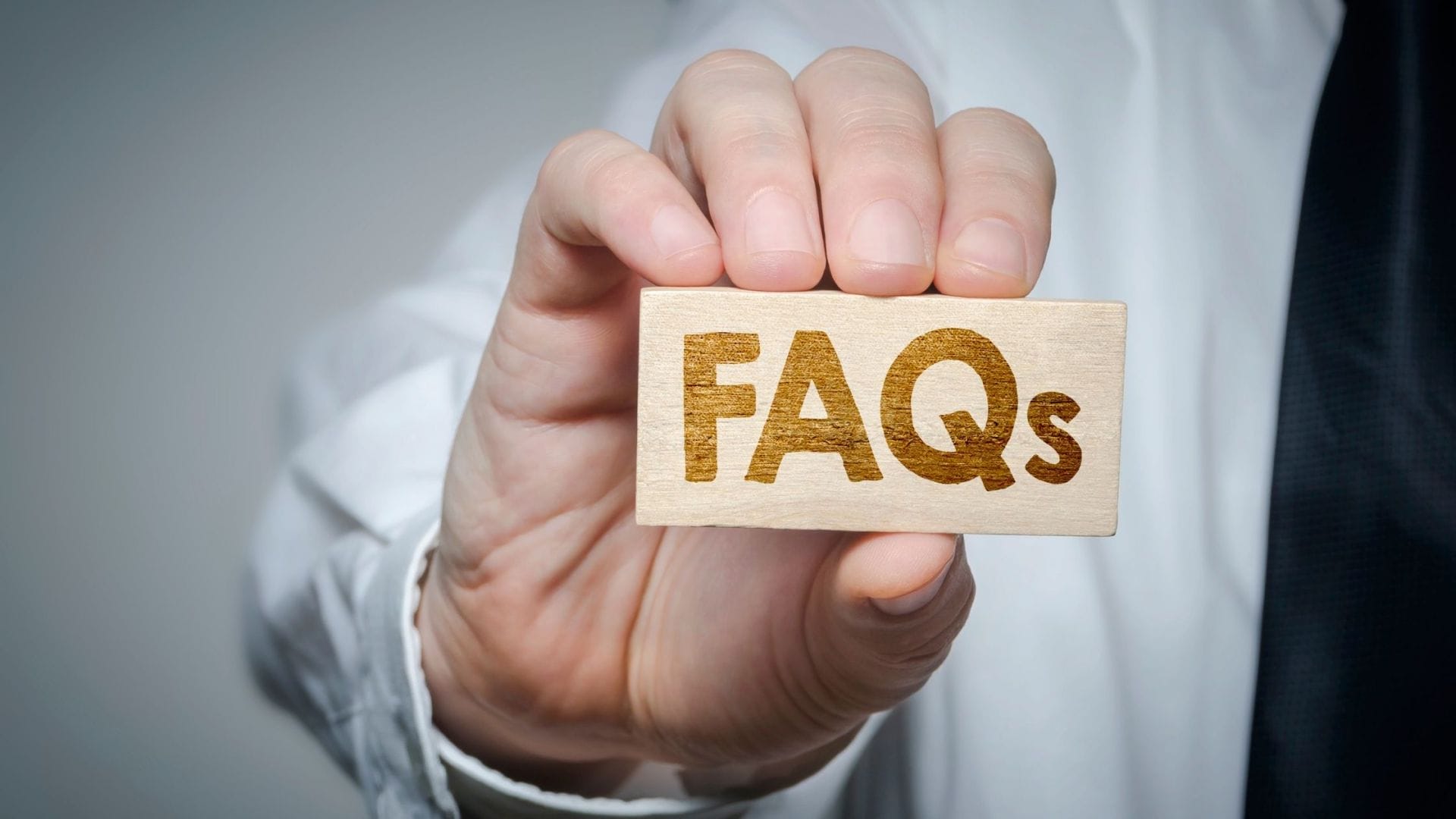 A person in business attire holding a wooden block with 'FAQs' inscribed on it, symbolizing frequently asked questions regarding the management of skin cancer treatment expenses.