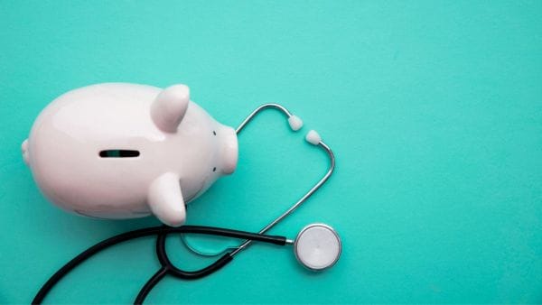 A white piggy bank with a stethoscope on a bright turquoise background, symbolizing the financial management of skin cancer treatment expenses.