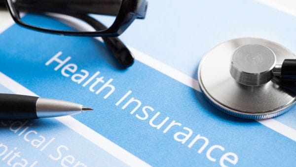 Close-up of a stethoscope and eyeglasses resting on a health insurance document, highlighting the importance of insurance in covering Sarcoma cancer treatment costs.